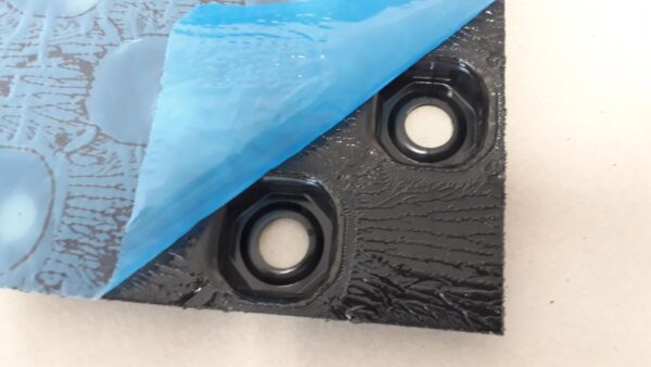 Sheet of black plastic castellated egg crate panel with secured pipe used for screed underfloor heating system