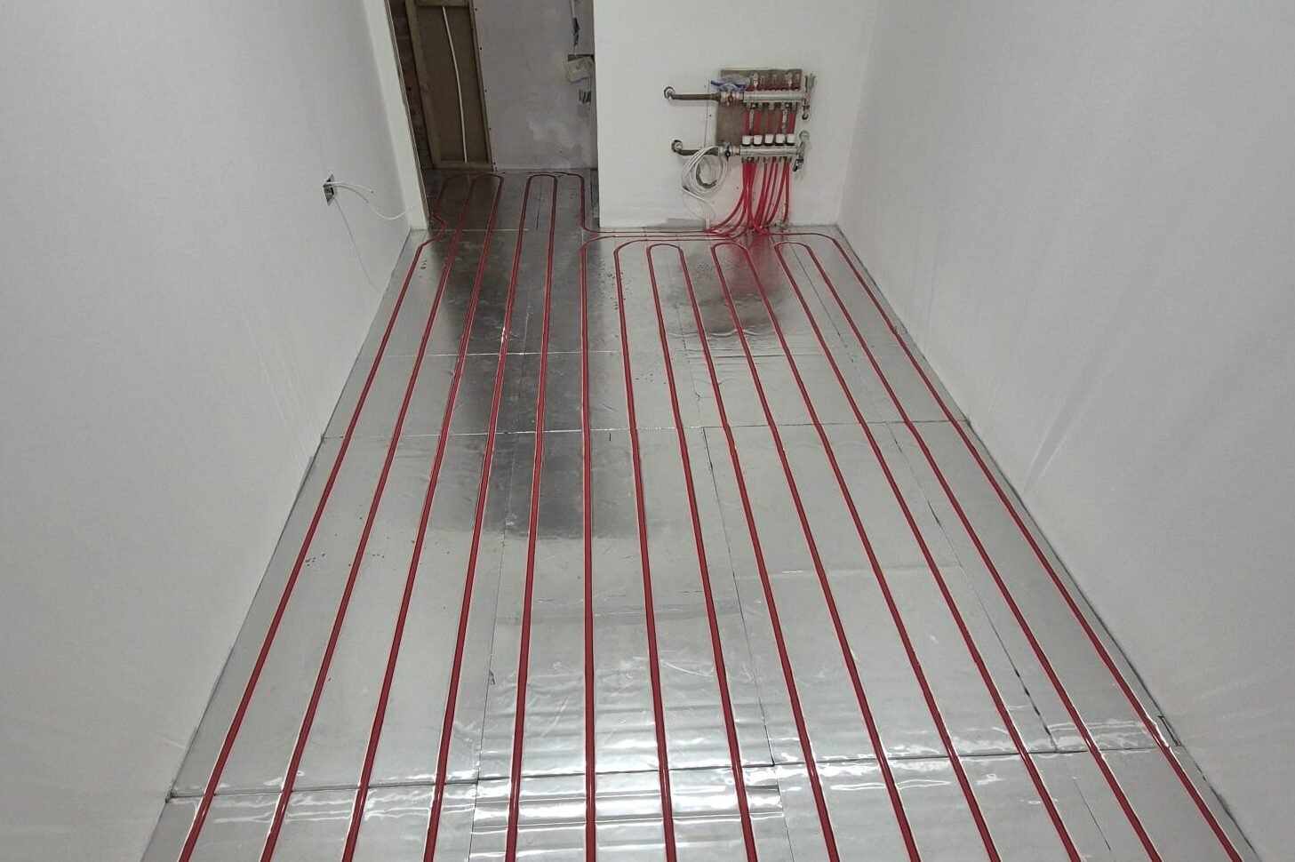 16mm red underfloor heating pipe installed on foil-faced insulation boards with manifold connection, demonstrating a water underfloor heating system layout.